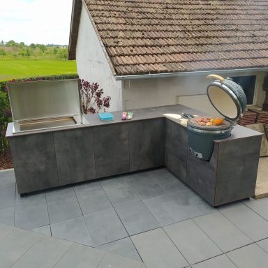 Moderne Außenküche mit Grill und Arbeitsfläche, umgeben von Rasen und Bäumen.