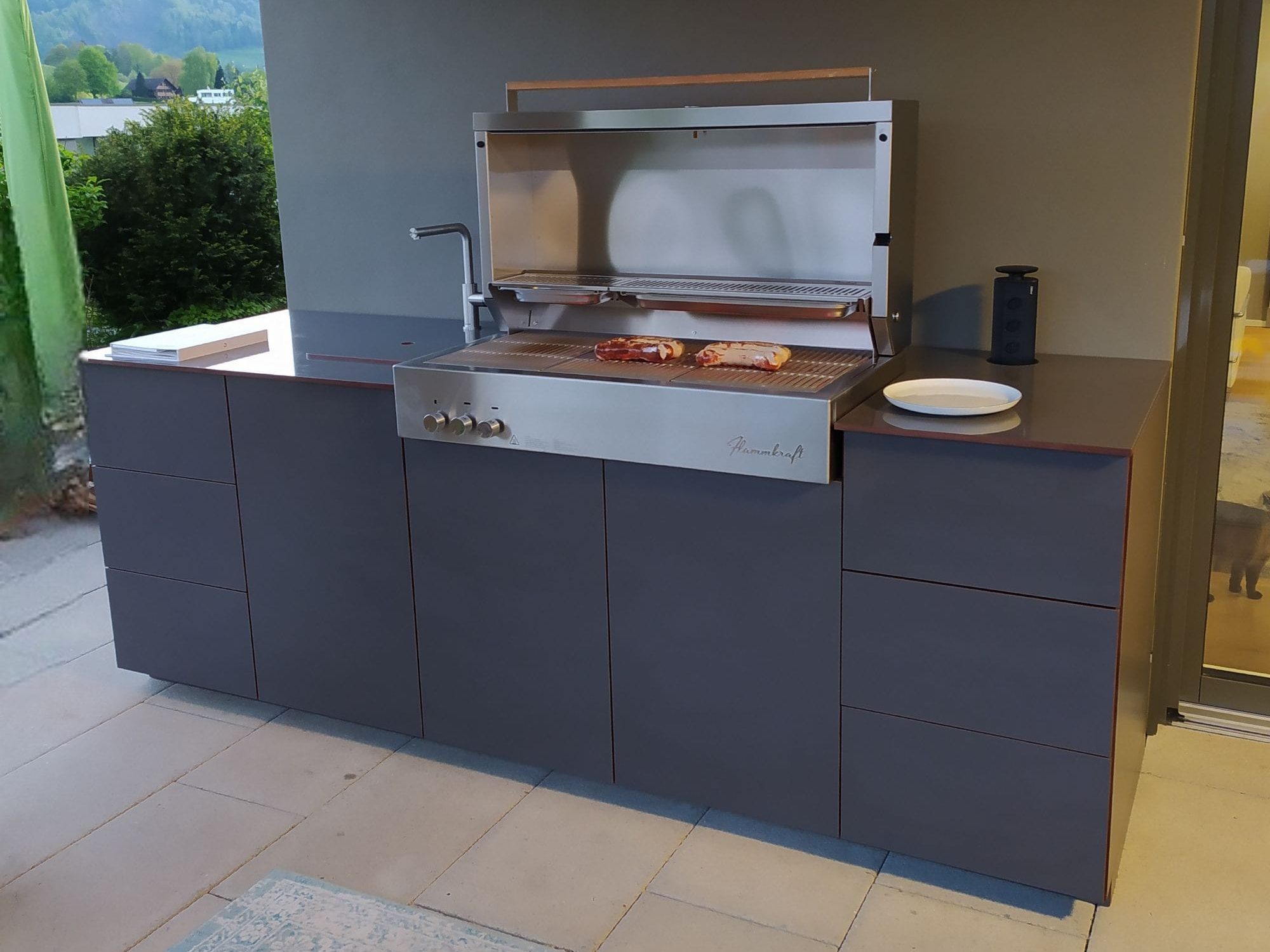 Moderne Außenküche mit Grill, Arbeitsfläche und Stauraum auf einer Terrasse.